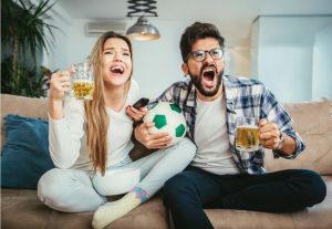 ζευγάρι στον καναπέ βλέπει ποδόσφαιρο και πίνει μπύρα